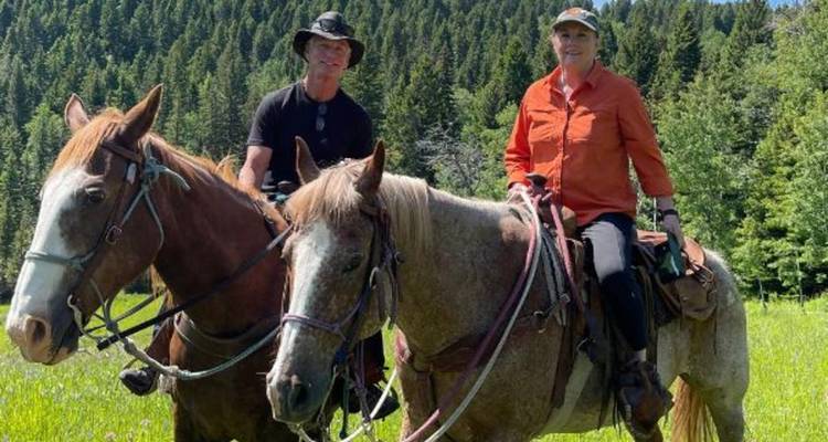 Deux cavaliers à cheval dans une prairie ensoleillée adossée à une forêt dense du Montana