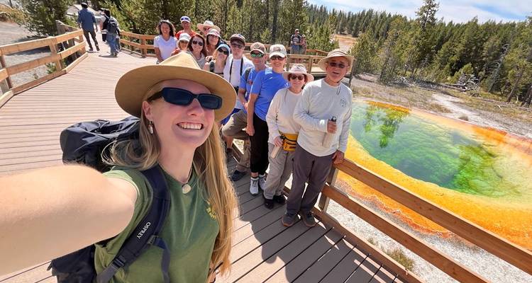 Groupe de touristes souriants prenant un selfie sur une promenade à côté de la piscine colorée Morning Glory Pool