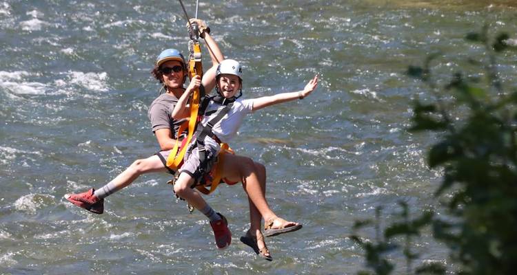 Un adulto y un niño disfrutando con emoción del tirolesa sobre un río que corre en Montana