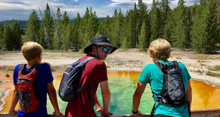 Tres adolescentes observan los colores arcoíris de una piscina termal desde una barandilla de madera