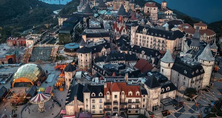 Luftaufnahme des europäisch gestalteten Bergresorts Ba Na Hills mit beleuchteten Burgen und Plätzen bei Dämmerung
