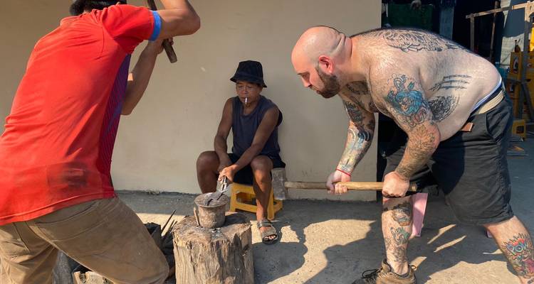 Un viajero tatuado y artesanos locales forjan metal sobre un yunque en el taller de la aldea.