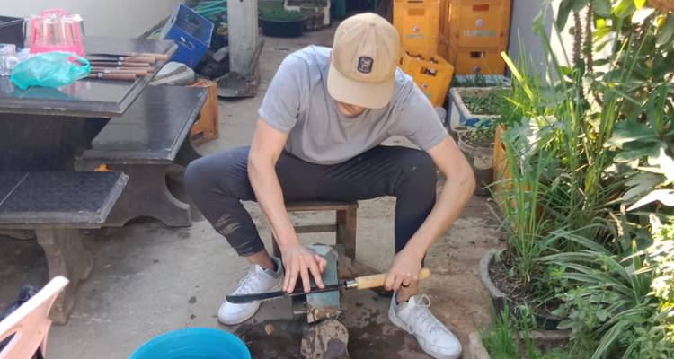 Un participante afila un cuchillo hecho a mano en una piedra de afilar afuera de un taller rural.