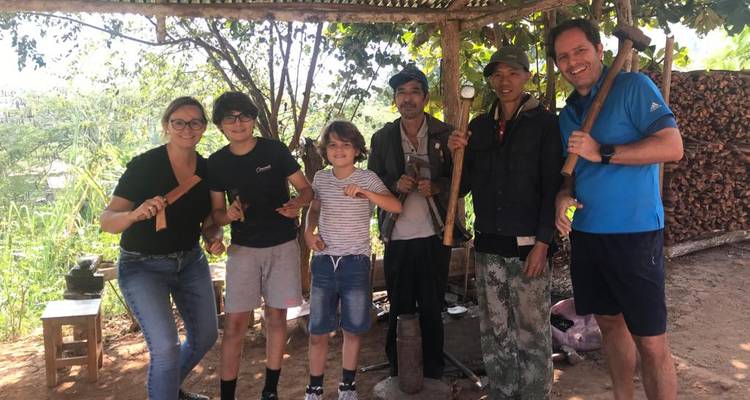 Turistas y artesanos locales sonriendo y posando con cuchillos hechos a mano bajo un refugio con sombra.
