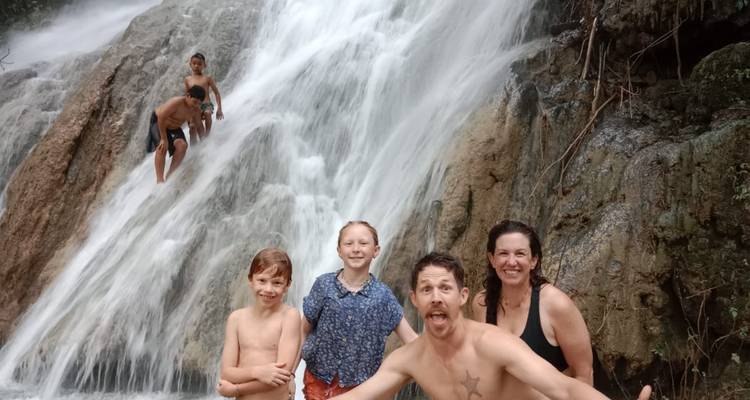 Familia sonriente posando frente a una cascada impetuosa mientras los niños trepan por las rocas de atrás