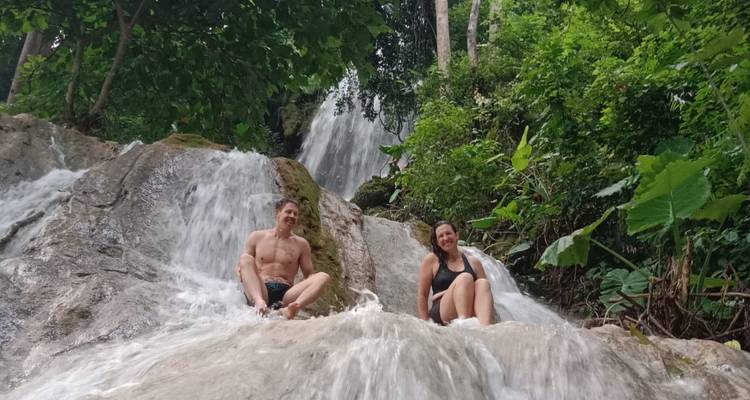 Hombre y mujer sentados en toboganes de roca lisa con agua fluyendo alrededor de ellos en una cascada de la selva