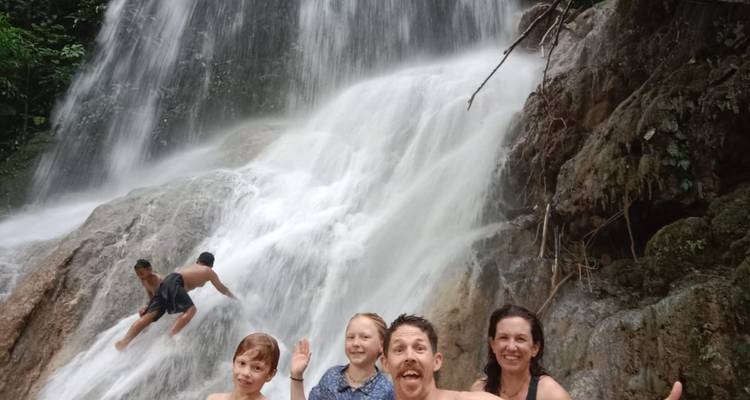 Una familia disfrutando del agua en la base de una cascada de selva mientras dos niños suben por las rocas