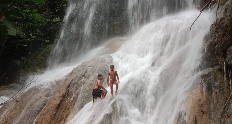Dos chicos parados en medio de la corriente en una cascada de varios niveles rodeada de selva