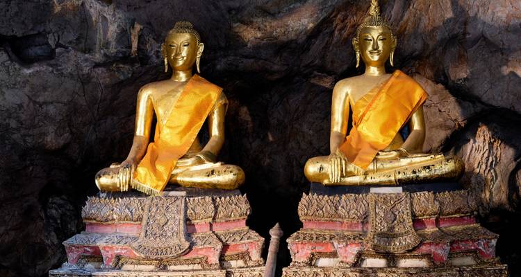 Zwei goldene Buddha-Statuen, die in der Pak-Ou-Höhle vor felsiger Kulisse sitzen