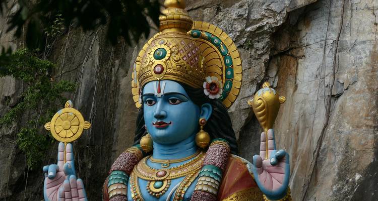 Lebhafte blaue Statue einer hinduistischen Gottheit mit verzierter goldener Krone vor einer Felswand