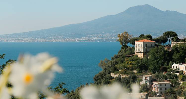 Blauwe zee en Mt. Vesuvius in de verte gezien vanaf een kustklif vol villa's en groen.