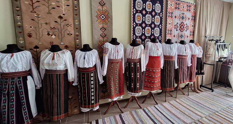 Rij van etalagepoppen gekleed in kleurrijke traditionele Moldavische kostuums tentoongesteld tegen gemusterde textiel achtergronden.