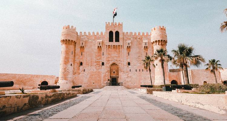 Vue de face de la Citadelle de Qaitbay fortifiée avec des palmiers et des canons