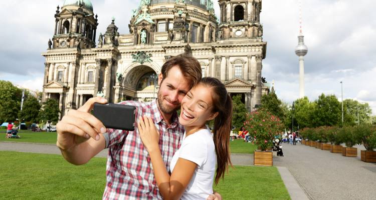 Pareja sonriente tomándose una selfie frente a la Catedral de Berlín con la Torre de Televisión elevándose detrás de ellos.