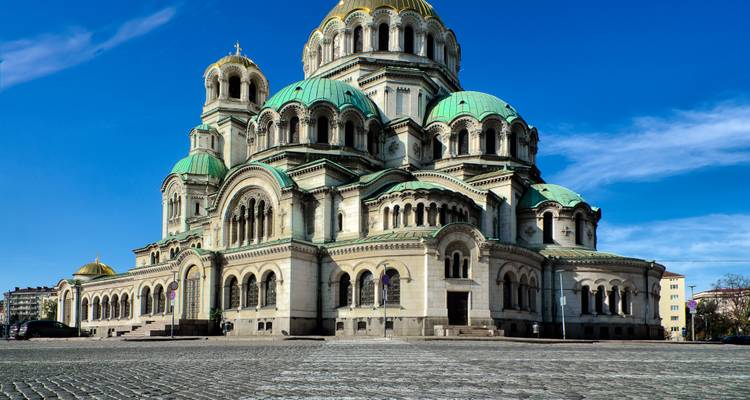 Majestueuze Alexander Nevsky Kathedraal met groene koepels en versierde bogen die schitteren onder een heldere blauwe hemel.
