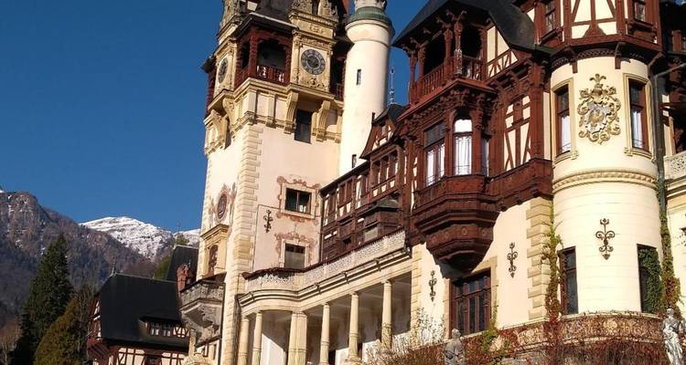 Fachada detallada y torre de reloj del Castillo de Peleș con montañas nevadas de fondo