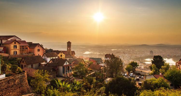 Amanecer dorado sobre Antananarivo con campanarios de iglesias y tejados recortados contra colinas brumosas.