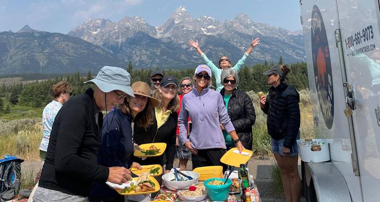 Déjeuner sur le bord de la route de style pique-nique où le groupe savoure des assiettes colorées de nourriture avec les pics dentelés spectaculaires de la chaîne de Teton en arrière-plan.