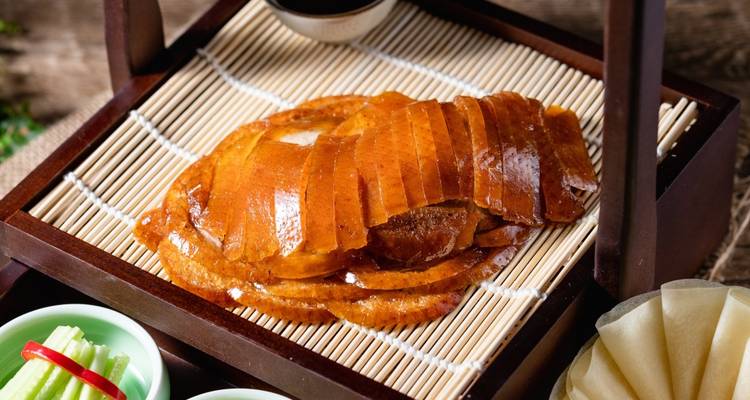 Mooi geschikt gesneden stukjes krokante Peking eend liggen op een bamboe dienblad naast traditionele sauzen en kruiden.