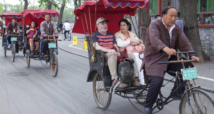 Toeristen rijden in traditionele riksja's door een historische Beijing hutong-straat, geleid door lokale chauffeurs.