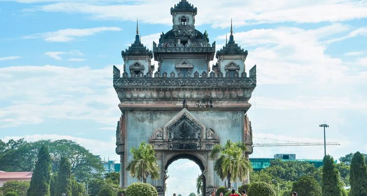 Der triumphale Patuxai-Bogen dominiert einen Boulevard mit Palmen und Besuchern, die umhergehen.