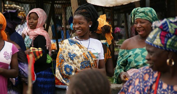 Lächelnde gambische Frauen in lebhaften traditionellen Stoffen auf einem belebten Markt