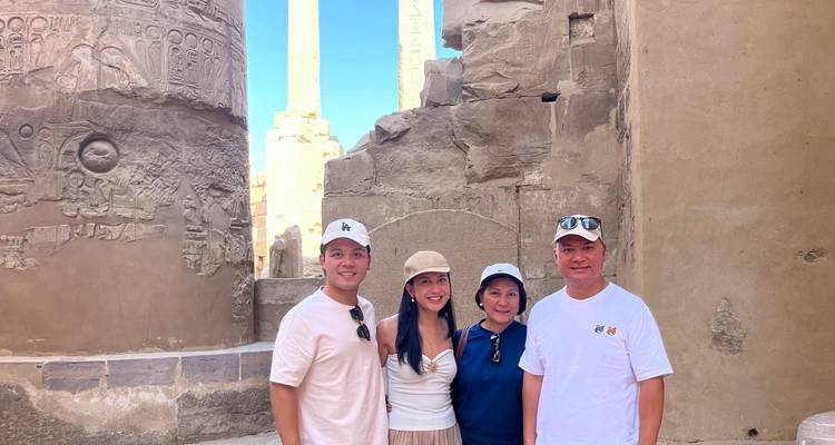 Une famille de quatre personnes pose parmi des colonnes hiéroglyphiques colossales et des obélisques dans un temple égyptien antique sous un ciel bleu dégagé.