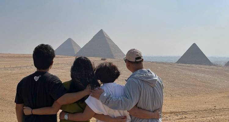 Quatre amis, les bras autour les uns des autres, admirent les pyramides de Giza depuis une crête sableuse.