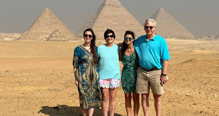 Une famille de quatre personnes posant ensemble avec les trois pyramides de Giza s'élevant du désert derrière eux.
