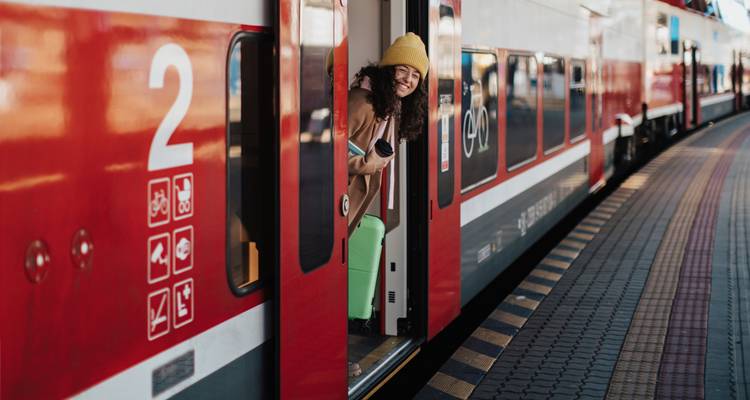 Smiling traveler leaning out of the doorway of a red and white passenger train at a station platform