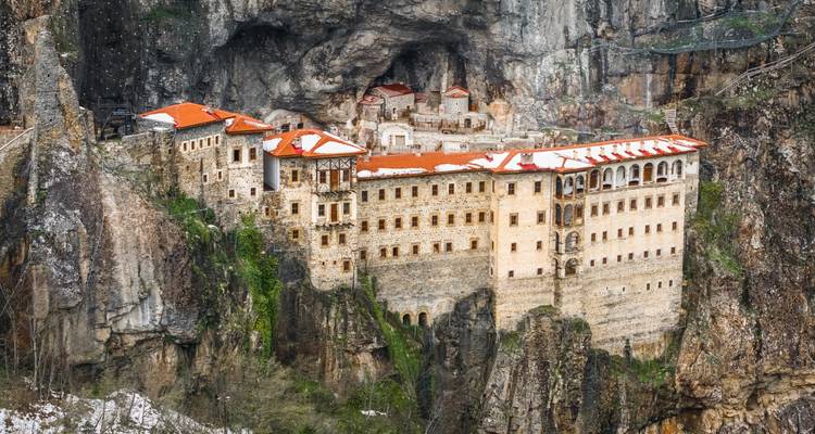 Historic Sumela Monastery with red-tiled roofs clinging to a dramatic cliff face amid rugged mountains