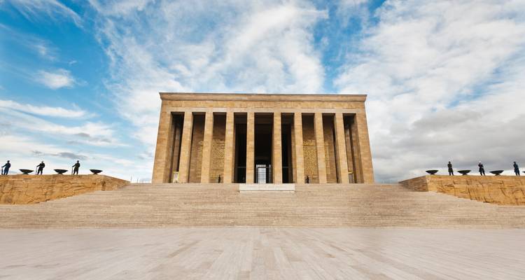 Symmetrical frontal view of Anitkabir mausoleum with tall columns against a dramatic cloudy sky