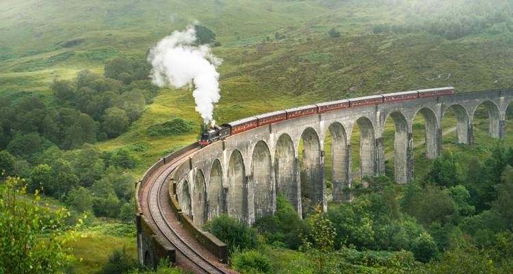 Steam locomotive crossing the curved arches of the Glenfinnan Viaduct amid lush green highlands