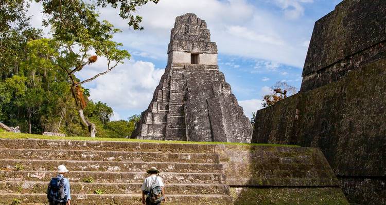 Deux voyageurs s'approchent de la pyramide emblématique de Tikal qui s'élève au-dessus des arbres de la jungle.