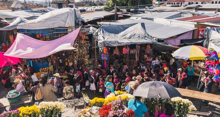 Vue aérienne d'un marché animé en altitude débordant de fleurs, d'artisanat et de bâches colorées.