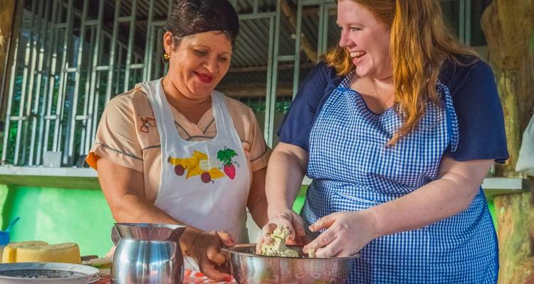 Local woman and traveler laughing together while kneading dough during a cooking workshop.