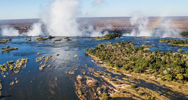 High viewpoint of the Zambezi River rushing toward Victoria Falls with mist and rainbow.