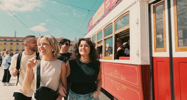 Groep vrolijke vrienden die langs een klassieke rode tram lopen op een zonnig stadsplein