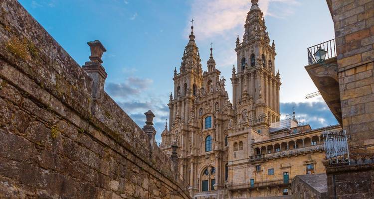 Las gemelas torres de la Catedral de Santiago de Compostela se alzan sobre las murallas de piedra antigua al atardecer.