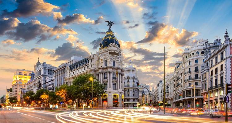 Los flujos de semáforos animan la Gran Vía de Madrid bajo nubes dramáticas que destacan las fachadas históricas.