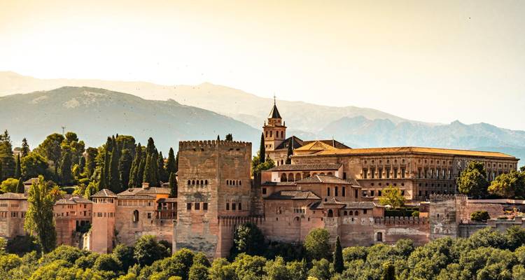 Les murs fortifiés et les palais de l'Alhambra se dressent majestueusement avec des toiles de fond montagneuses dans la douce lumière du soir.
