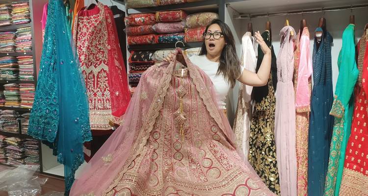 Enthousiaste shopper die een ingewikkelde roze lehenga vasthoudt in een kleurrijke textielwinkel.