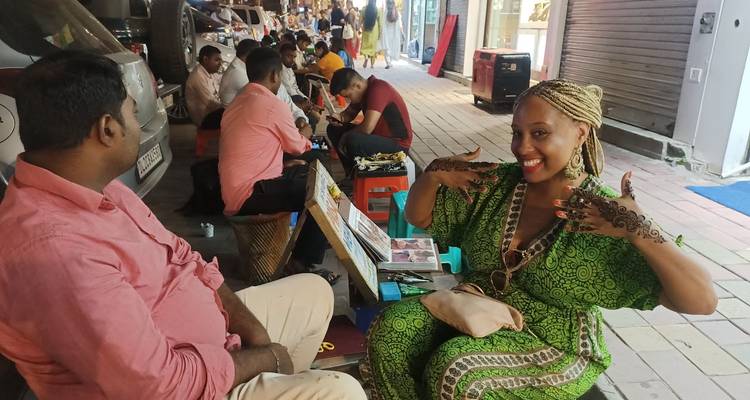 Toerist die glimlacht terwijl er ingewikkelde henna op een druk straatmarkt wordt aangebracht.