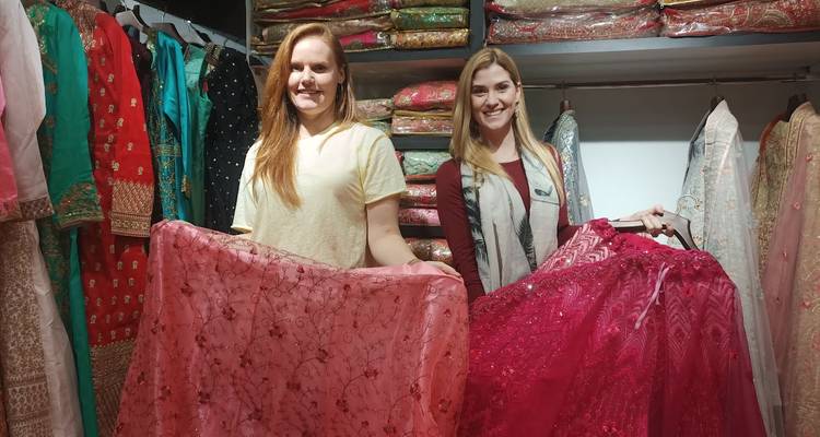 Twee vrouwen die glimlachen terwijl ze kleurrijke stoffen vasthouden in een kledingboutique.
