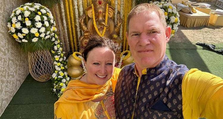 Gelukkig stel gekleed in traditionele gele kleding die een selfie maakt voor een fraai versierde Ganesha-standbeeld met bloemen.