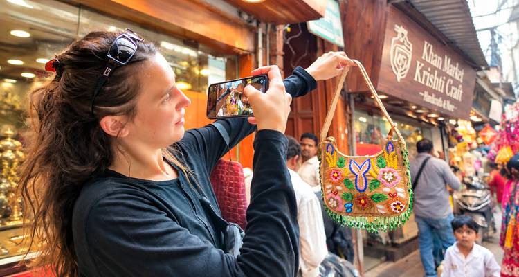 Jonge vrouw die een kleurrijke geborduurd handtas fotografeert op een drukke Indiase straatmarkt.