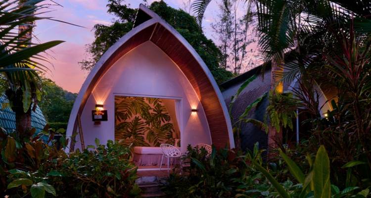 Encantador bungaló con techo curvo rodeado de exuberantes plantas de la selva al atardecer.