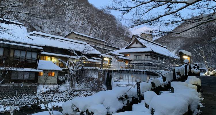 Traditionelle Holz-Onsen-Stadt bedeckt mit Neuschnee neben einem Bergfluss in der Dämmerung.