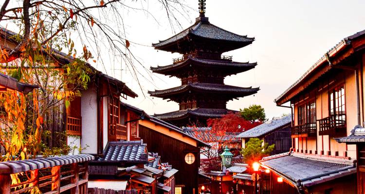Die ikonische fünfstöckige Yasaka-Pagode erhebt sich über schmale, laternenbeleuchtete Gassen und Herbstbäume in der Dämmerung.