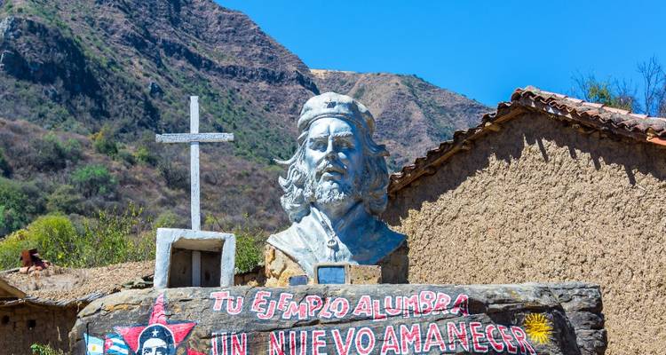 Busto de Che Guevara con montañas de fondo y un mural revolucionario colorido